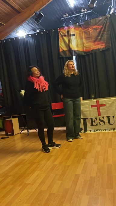 Twee power vrouwen staan op een podium naast een banner met de tekst "JESUS".