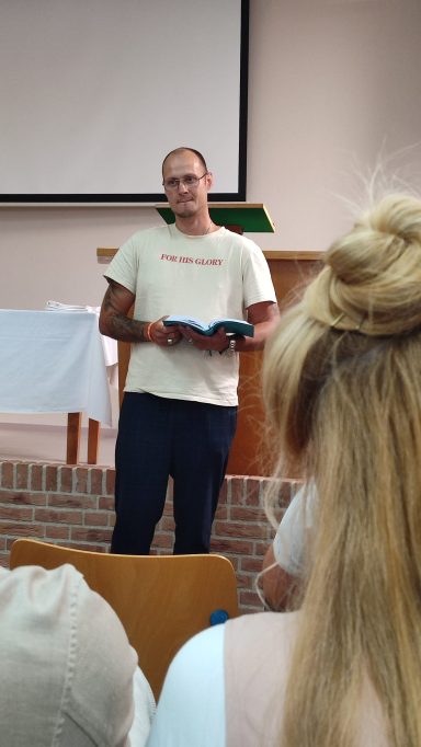 Man leest uit een boek tijdens een bijeenkomst in een zaal.